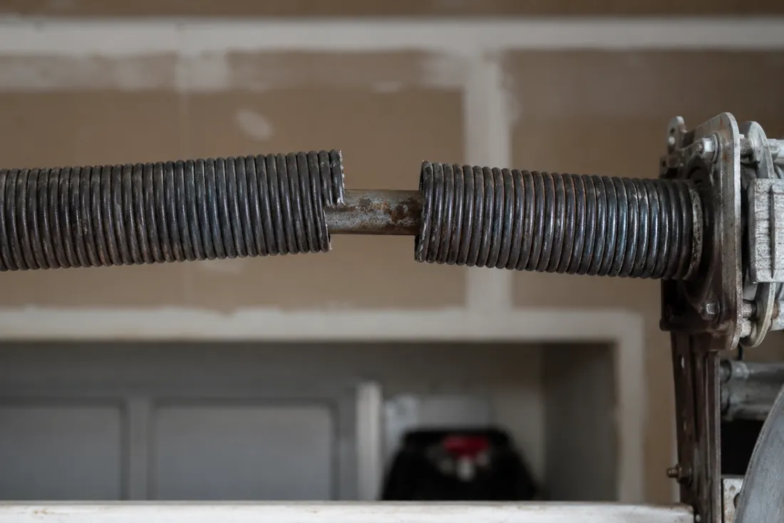 Broken garage door torsion spring on the steel shaft, showing a clear gap in the coil
