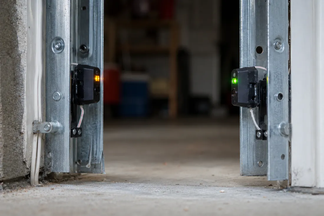 Two garage door photo-eye sensors mounted near the floor, one glowing amber and one green