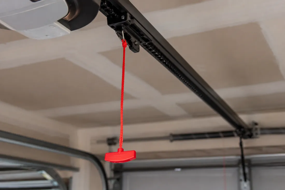 Red emergency-release cord and handle hanging from a garage door opener rail